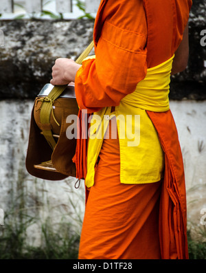 LUANG PRABANG, Laos: Monaci buddisti e novizi in luccicanti accappatoi di zafferano camminano in un unico file per le strade di Luang Prabang durante la cerimonia di consegna delle elemosine del mattino presto nota come tak bat. La gente del posto e i turisti si allineano lungo il percorso, offrendo cibo in questo rituale quotidiano che è centrale per la tradizione buddista del Laos. Foto Stock