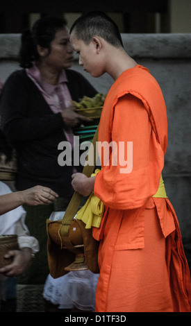 LUANG PRABANG, Laos: Monaci buddisti e novizi in luccicanti accappatoi di zafferano camminano in un unico file per le strade di Luang Prabang durante la cerimonia di consegna delle elemosine del mattino presto nota come tak bat. La gente del posto e i turisti si allineano lungo il percorso, offrendo cibo in questo rituale quotidiano che è centrale per la tradizione buddista del Laos. Foto Stock