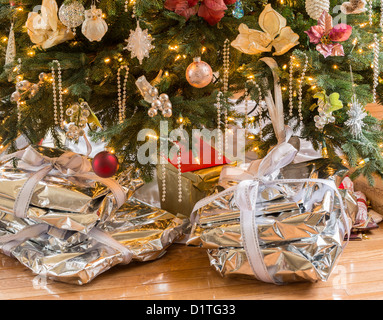 Presenta avvolto in carta argentata e nastri al di sotto dell albero di Natale sul pavimento in legno Foto Stock