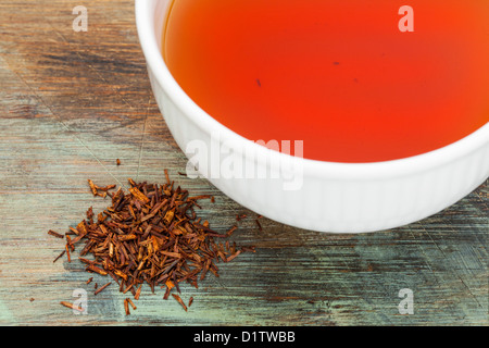 Rooibos tè rosso - bianco una tazza di bevanda e foglie staccate su uno sfondo di legno, tè realizzato dal sudafricano boccola rossa Foto Stock