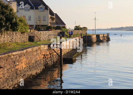 Due persone facendo una passeggiata serale lungo il lungomare seawall dalla Stretto di Menai a Y Felinheli, Gwynedd, Galles del Nord, Regno Unito Foto Stock