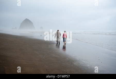 Giovane camminando lungo la spiaggia a Cannon Beach verso Haystack Rock, STATI UNITI D'AMERICA Foto Stock