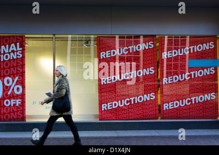 Moto donna sfocata passando riduzioni poster nella finestra di Primark, Bromley. Foto Stock