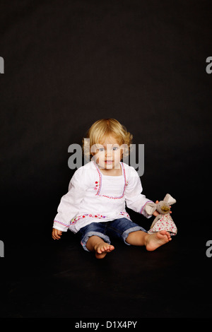 Due anni di età infantile bionda ragazza in camicia bianca e denim su sfondo nero Foto Stock