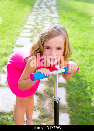 Bambino felice ragazza che gioca con gli scooter in giardino sorridenti Foto Stock