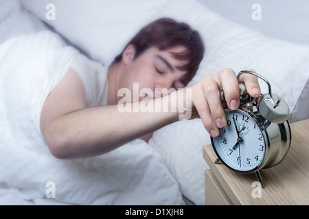 In prossimità di un vecchio orologio sveglia, giovane uomo a spegnere ancora mezzo addormentato. Foto Stock