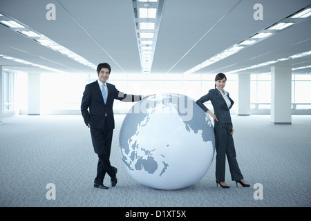 Un imprenditore e la donna appoggiato su di un enorme globo in una stanza vuota Foto Stock