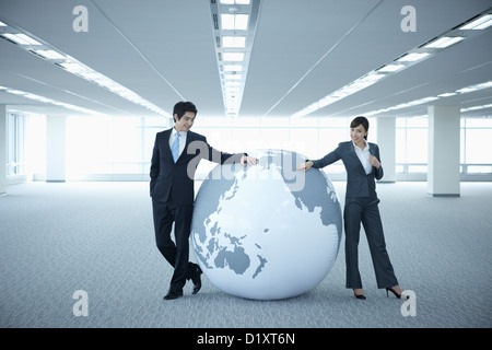 Un imprenditore e la donna appoggiato su di un enorme globo in una stanza vuota Foto Stock