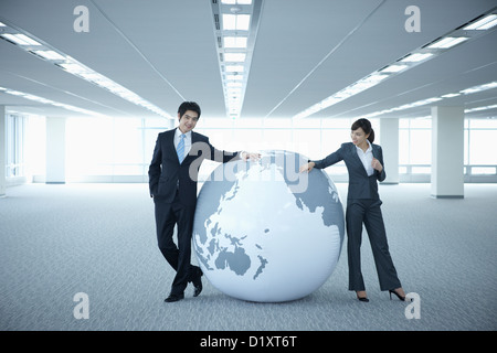 Un imprenditore e la donna appoggiato su di un enorme globo in una stanza vuota Foto Stock