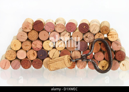 Vecchio cavatappi con un tappo di sughero su di esso contro la pila di vino utilizzati tappi in sughero con la riflessione in un tavolo di vetro Foto Stock