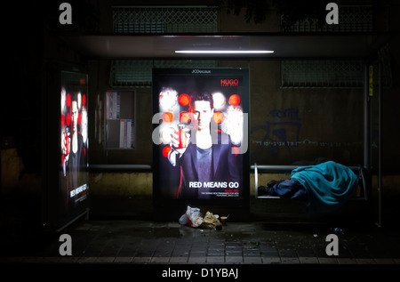 Una persona senza tetto che dorme in una stazione degli autobus a Rothschild via di notte a Tel Aviv Israele Foto Stock