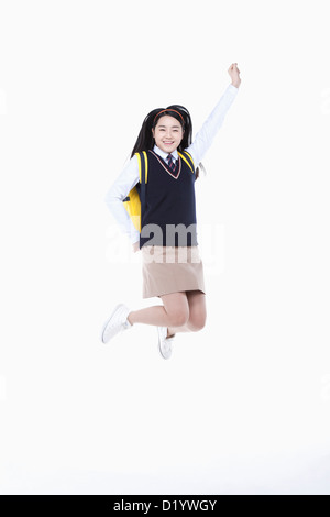 Una studentessa con la scuola uniforme e un sacco di scuola jumping mentre sollevando il suo braccio Foto Stock