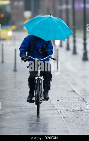 Un ciclista cerca di proteggere se stesso dalla pioggia con un ombrello a Berlino, Germania, 09 gennaio 2013. Foto: MAURIZIO GAMBARINI Foto Stock