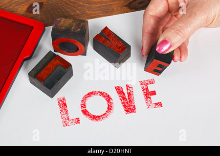 Una donna con stampa in rilievo in legno blocchi per stampare la parola AMORE in inchiostro rosso su carta bianca. Foto Stock