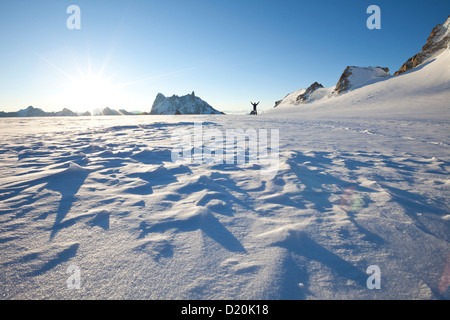 Uomo i bracci di sollevamento sul Col du Midi di sunrise, affacciato su Les Grandes Jorasses e Dent du Geant, Chamonix Mont Blanc, Francia, Eur Foto Stock