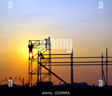 Lavoratori edili in alto su una impalcatura visto contro il sole di setting Foto Stock
