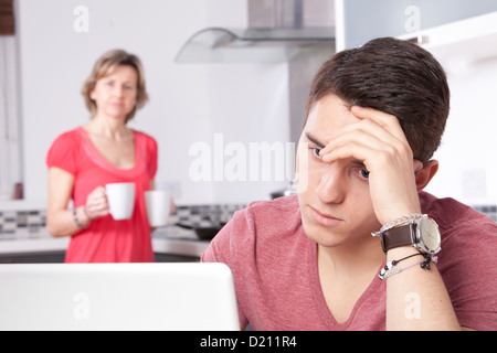 Uomo Worri utilizzando una tavoletta digitale guardando lo schermo o monitor. Impostare in una cucina moderna con una donna con 2 tazze guarda interessate Foto Stock