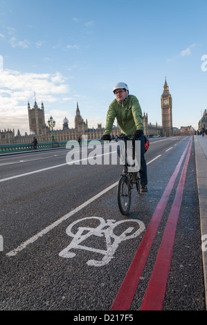 Un ciclista in sella sulla strada sopra Westminster Bridge London REGNO UNITO mostra pista ciclabile e doppie linee rosse, il Parlamento in background. Foto Stock