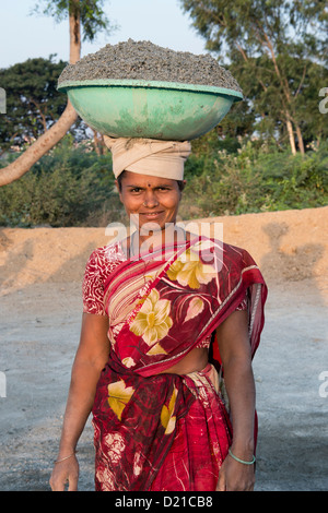 Donna indiana che trasportano calcestruzzo in una ciotola sul suo capo e allo stesso tempo di rendere i blocchi di calcestruzzo. Andhra Pradesh, India Foto Stock