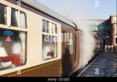 La sala con il treno alla stazione di seppellire sulla East Lancashire Railway. Il vapore è il riscaldamento delle carrozze prima ai passeggeri di salire a bordo. Foto Stock