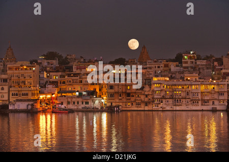 La luna piena sorge su una chiara notte sulla città e templi di Udaipur, India con riflessi nel lago Pichola Foto Stock