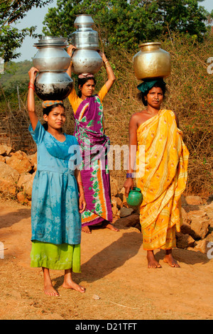 Tribeswomen colorati che trasportano acqua tradizionali pentole in un villaggio vicino a Jeypore nel sud dell Orissa, India. Foto Stock