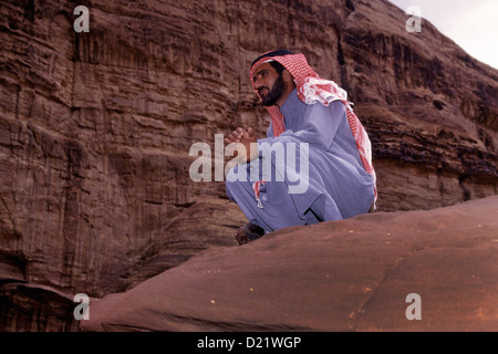 Giordani un uomo seduto su una scogliera che indossa keffiyeh o kufiyain noto anche come ghutrah araba tradizionale copricapo in Khazali Canyon Wadi Rum desert conosciuta anche come la Valle della Luna in Giordania Meridionale Foto Stock