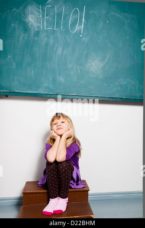 Studio Ritratto di giovane sorridente ragazza seduta in aula con la parola hello scritta sulla lavagna Foto Stock