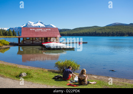 Giovane seduto sulla banca del Lago Maligne con il boathouse nel Parco Nazionale di Jasper in Alberta Canada Foto Stock