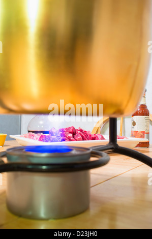 La fonduta di carne vaso riempito con olio di riscaldamento sulla fiamma aperta dal can del combustibile di cottura, un piatto di carne cruda in background Foto Stock