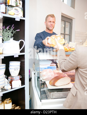 Un assistente in un negozio di specialità gastronomiche offre una pagnotta di pane a un cliente Foto Stock