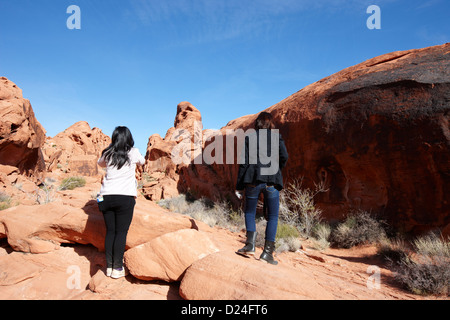 Due femmina turisti asiatici a piedi fino al rock coperto di petroglifi mouse lungo il sentiero del serbatoio della valle del fuoco del parco statale nevada usa Foto Stock