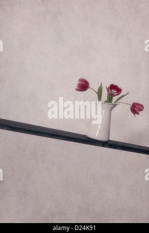 Tre i tulipani in un vaso su un lopesided tagliere in legno Foto Stock