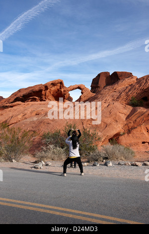 Due femmina turisti asiatici pongono e scattare foto di fronte arch rock in il parco della Valle di Fire State nevada usa Foto Stock