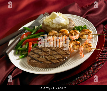 Bistecche e spiedini di gamberi cena caricato con patate al forno e verdure Foto Stock