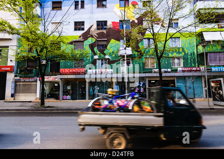 Il triciclo van passando rapidamente da un cavallo con fantino pittura murale nel centrale quartiere Blloku di Tirana , Albania Foto Stock