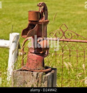 Un vecchio arrugginito pompa acqua con il proprio stagno arrugginito mug. Foto Stock