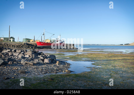 Seascape guardando oltre il molo a bassa marea con barca da pesca sulle rocce. Foto Stock