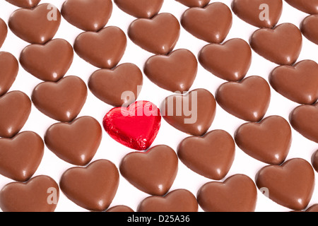 Righe di Cioccolato cuori con uno strano uno ancora in essa rosso di involucro in foglio, sfondo bianco. Foto Stock