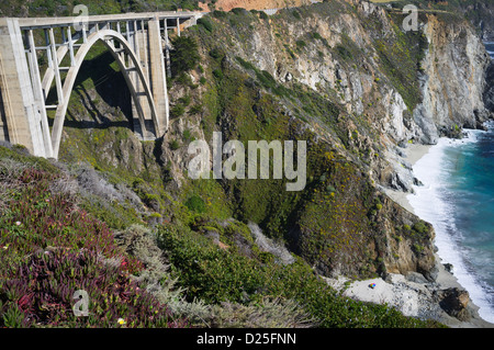 Bixby Creek Ponte sul Big Sur Hwy 1 strada costiera. Sunbather sulla spiaggia sottostante ponte sdraiati sotto l ombrello Foto Stock