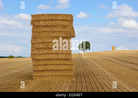 Un paesaggio estivo con un alta pila di balle di paglia in un campo di stoppie dorata sotto un cielo blu con nuvole soffici Foto Stock