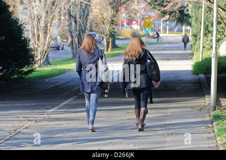 Due giovani donne caucasici con capelli lunghi marrone che trasportano le borsette marciando nella fase insieme sul marciapiede, Heilbronn Germania Foto Stock