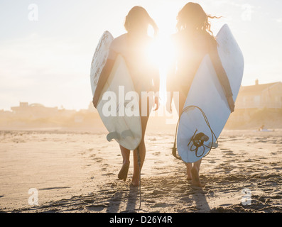 Stati Uniti d'America, nello Stato di New York, Rockaway Beach, due femmina surfers camminando sulla spiaggia al tramonto Foto Stock