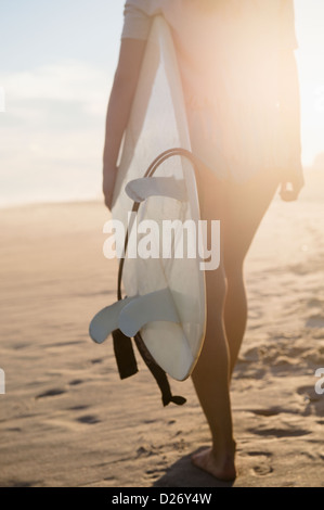 Stati Uniti d'America, nello Stato di New York, Rockaway Beach, Femmina surfer camminando sulla spiaggia al tramonto Foto Stock
