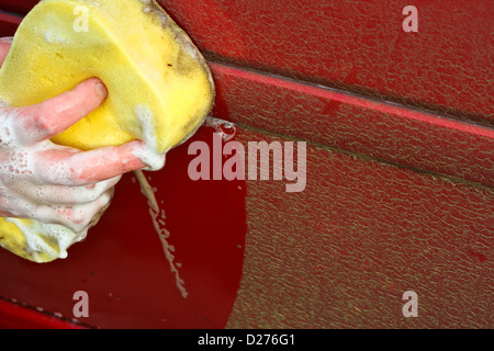 La pulizia della macchina sporca a mano con un giallo spugna saponata meglio di lavaggio automatico Foto Stock