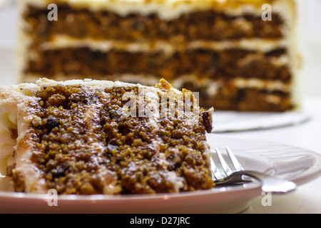 Primo piano della fetta di torta di carote su una piastra con forcella con mezza torta in prossimita' in background Foto Stock