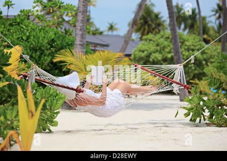 Donna rilassante in un amaca e la lettura di un libro su una spiaggia delle Maldive Foto Stock