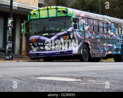 Viola e verde graffiti scuola bus con monster ganasce dipinta sulla fiancata, seduto su un Oriente Austin street Foto Stock
