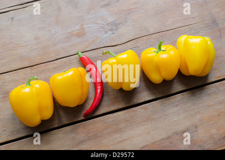 Fila di dolce peperone giallo e uno rosso peperoncino piccante tra di loro su vintage tavolo in legno Foto Stock