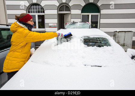 La donna pulisce la sua auto da ghiaccio e neve. Foto Stock